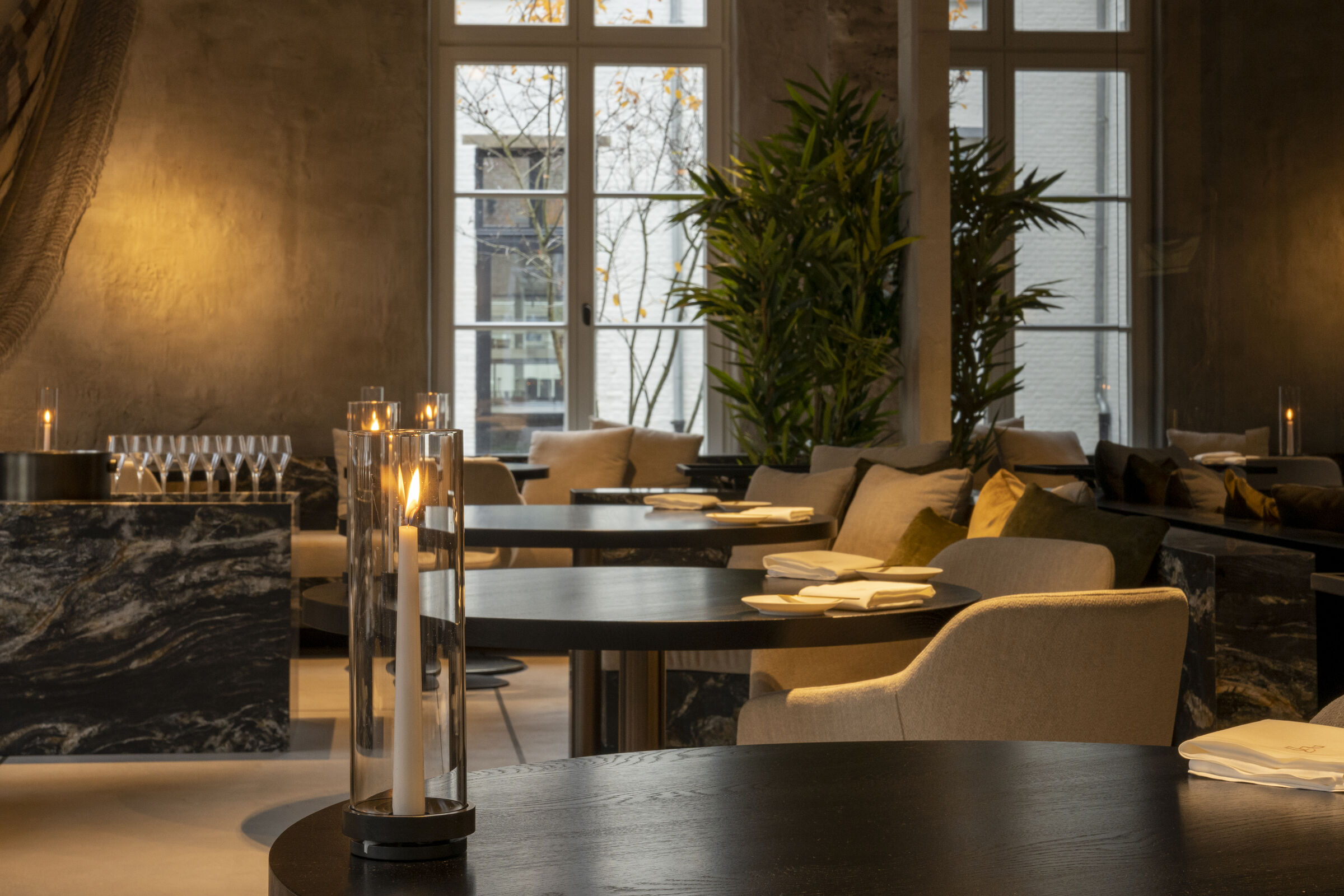 De eetzaal van Fine Fleur met een marmeren tafel, kaarsen en hoge ramen