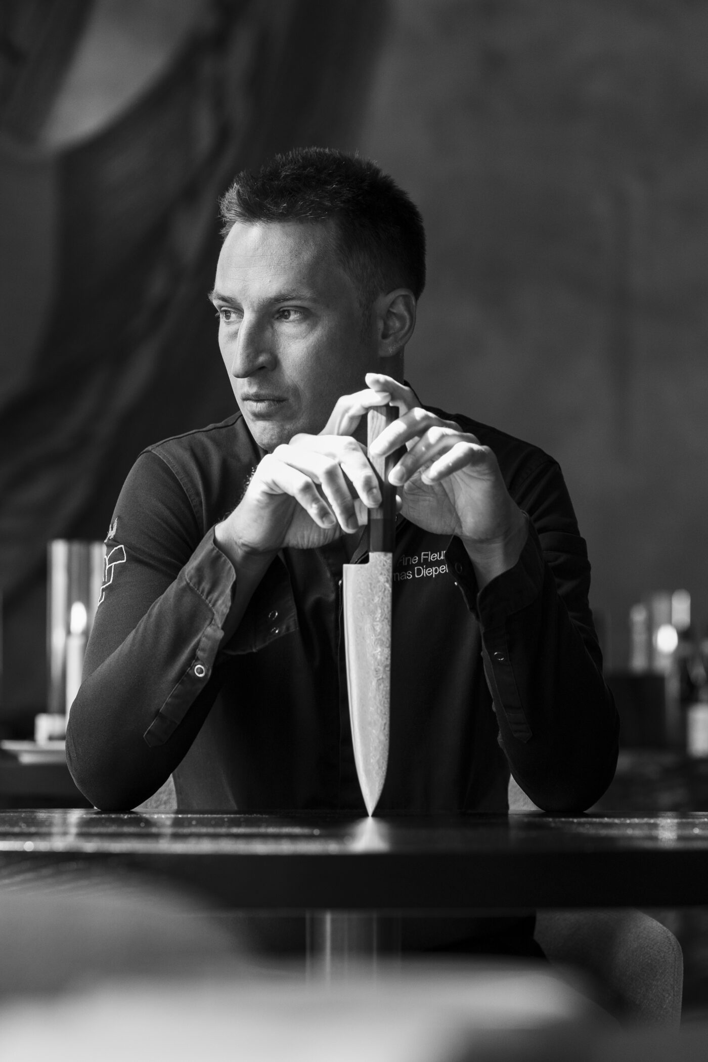 Thomas Diepersloot zit aan een tafel met zijn koksmes rechtop tussen de handen